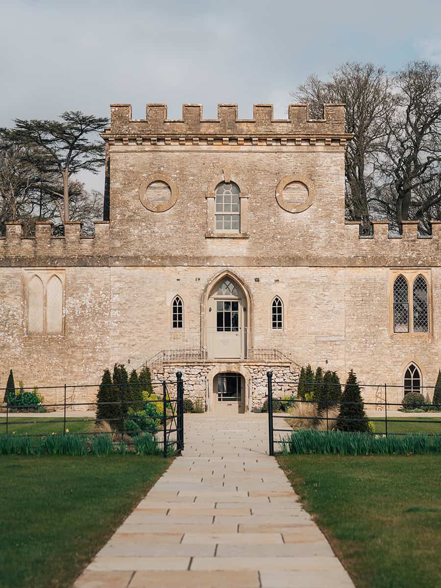 Ivy Lodge castellated stone facade with Gothic arched entrance and pathway, Cirencester Park Cotswolds